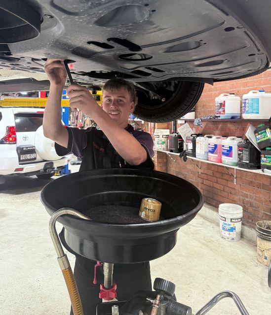 A Newcastle Mechanic draining oil from a car on a lift into a black oil pan in the workshop — AutoHop Lambton in Lambton, NSW