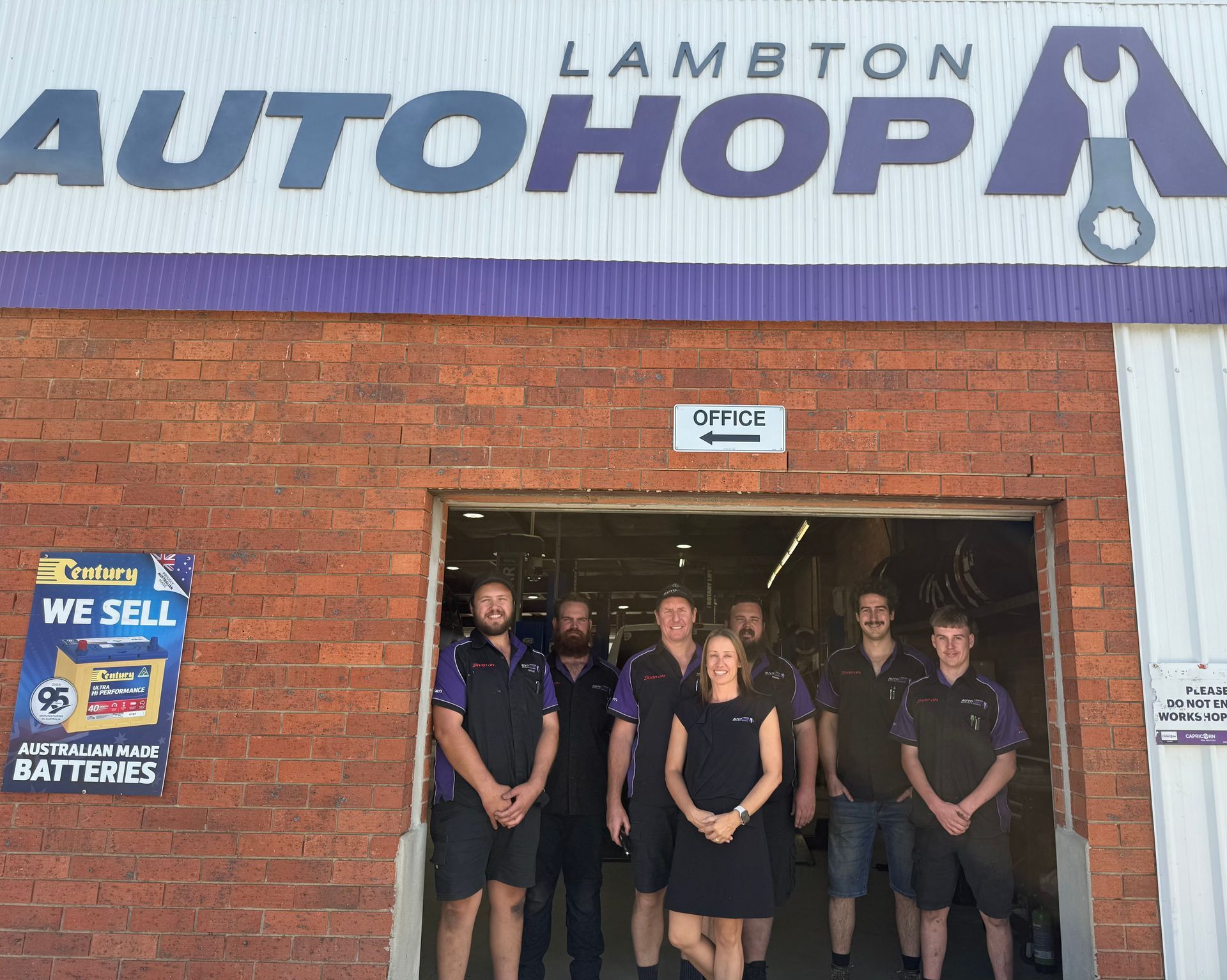 A team of Qualified Mechanics in Newcastle wearing black and purple uniforms in front of the AutoHop Lambton workshop