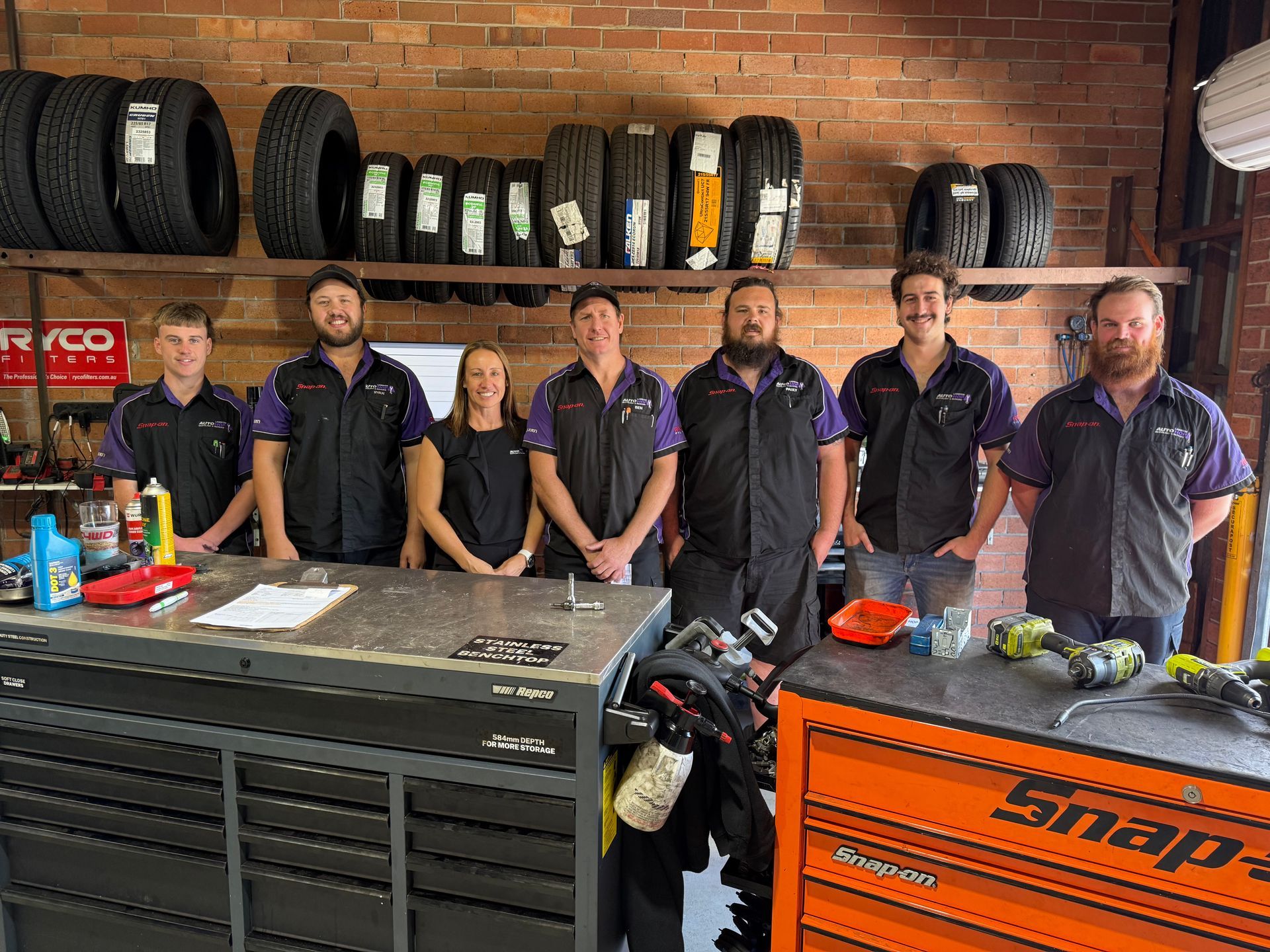 Six People in Matching Work Uniforms Stand in Front of A Brick Building with A Garage Door — AutoHop Lambton in Lambton, NSW