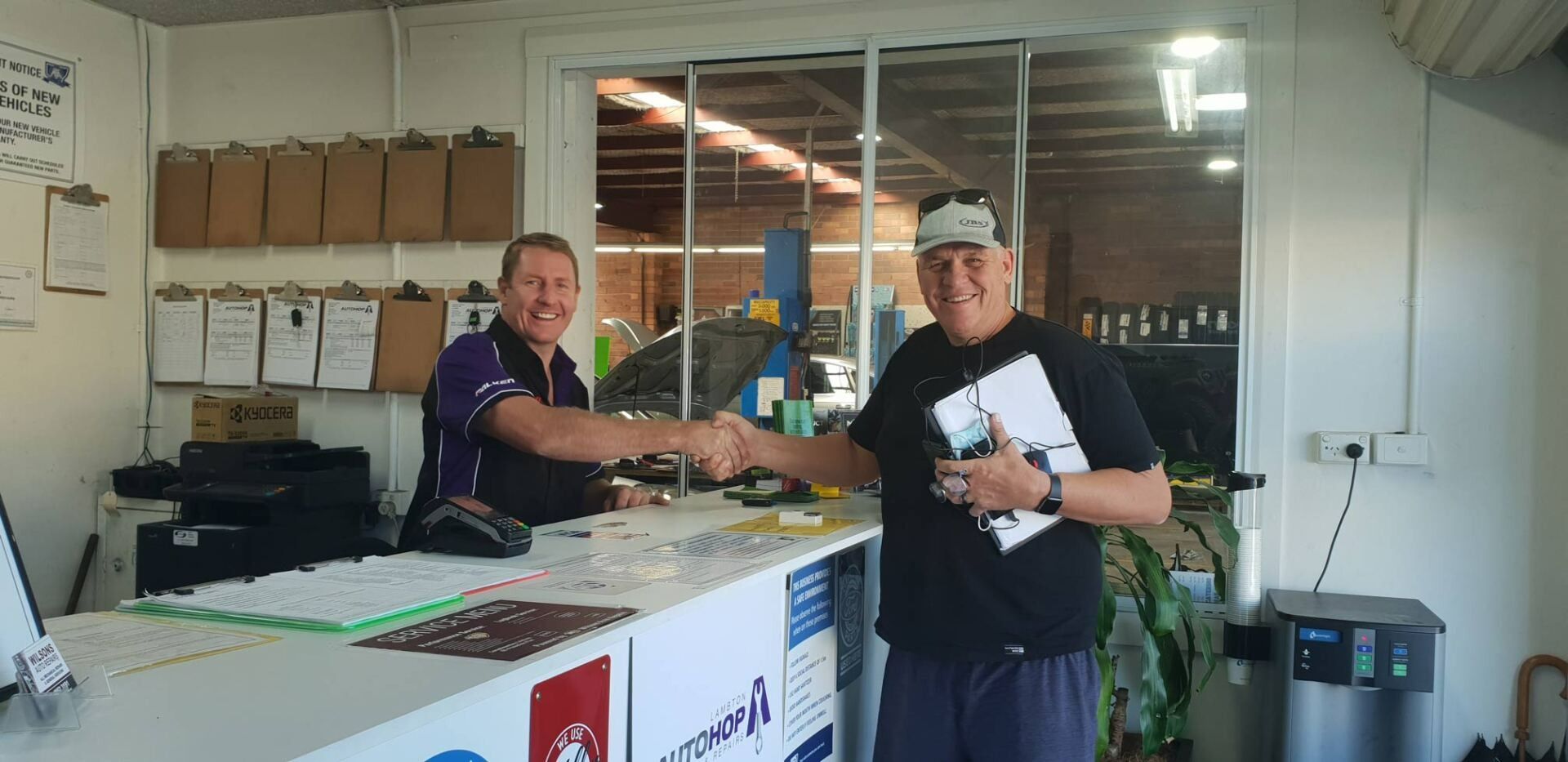 Two Men Shake Hands Over a Counter Inside a Shop — AutoHop Lambton in Lambton, NSW