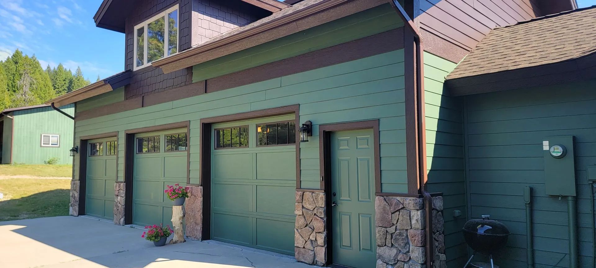 Green garage doors on a house exterior with a small entry door and dormer windows under a brown roof