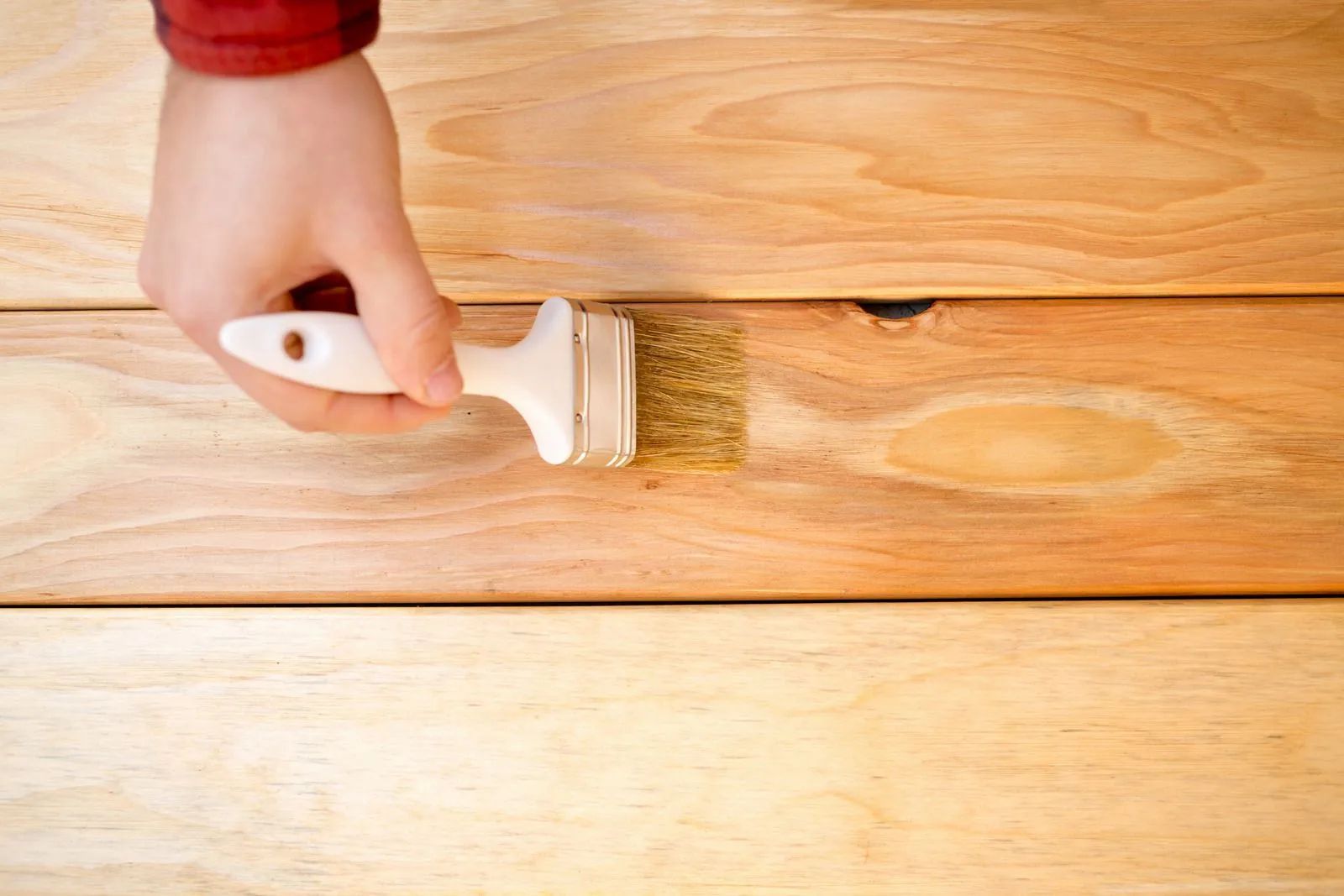 A hand brushes stain onto wooden planks, enhancing their color.