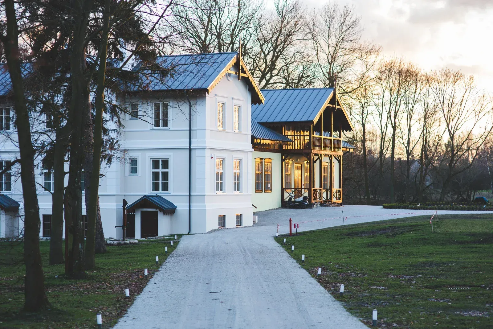 White house with blue roof and glass porch at dusk, reached by a paved path through leafless trees