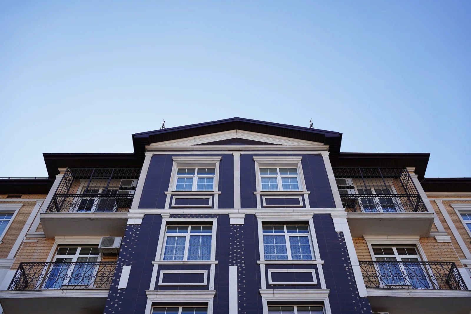 Symmetrical blue-and-white apartment building viewed from below against a clear sky