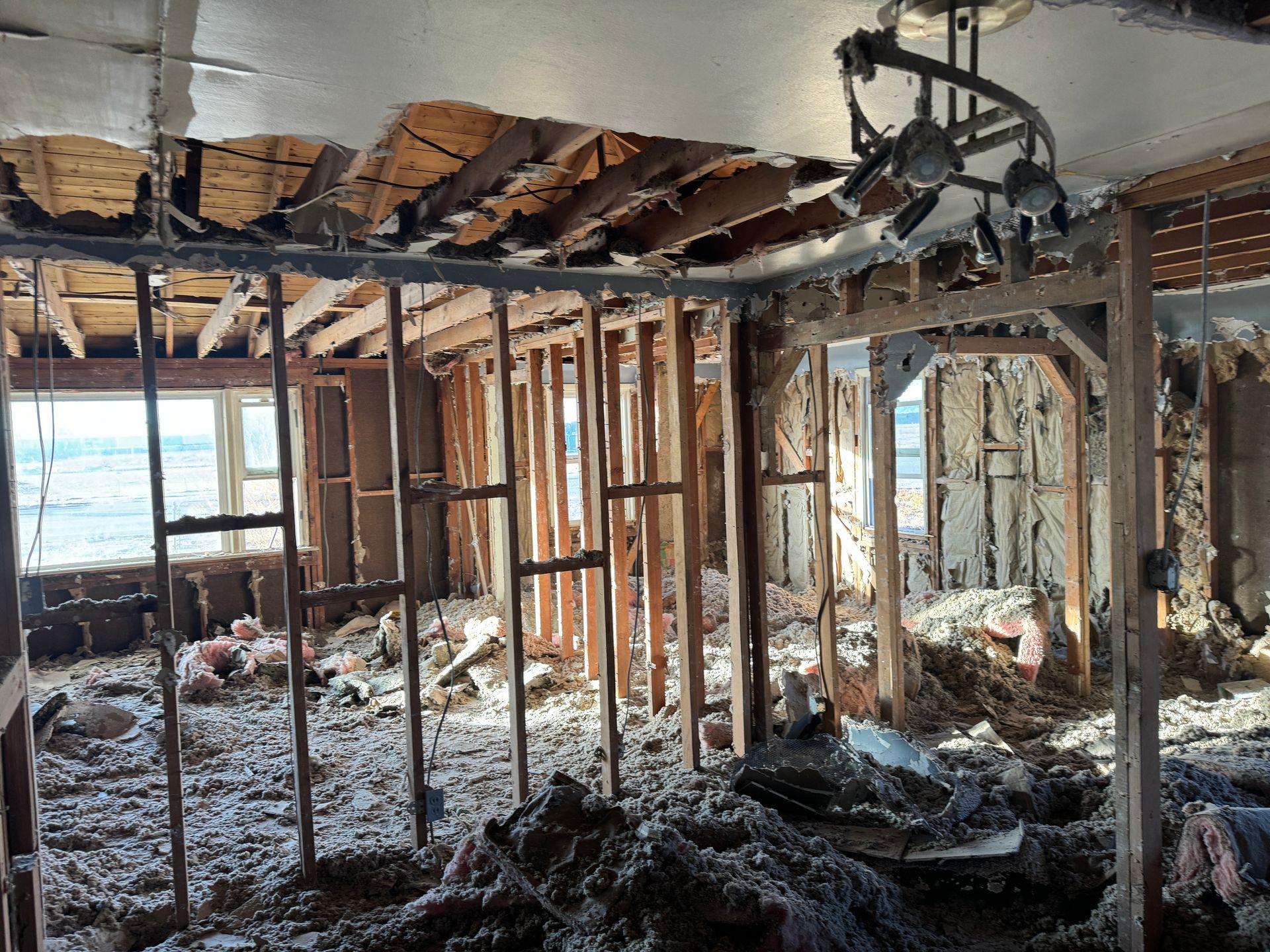 Interior of a building damaged by fire, showing exposed studs, insulation, and collapsed ceiling.