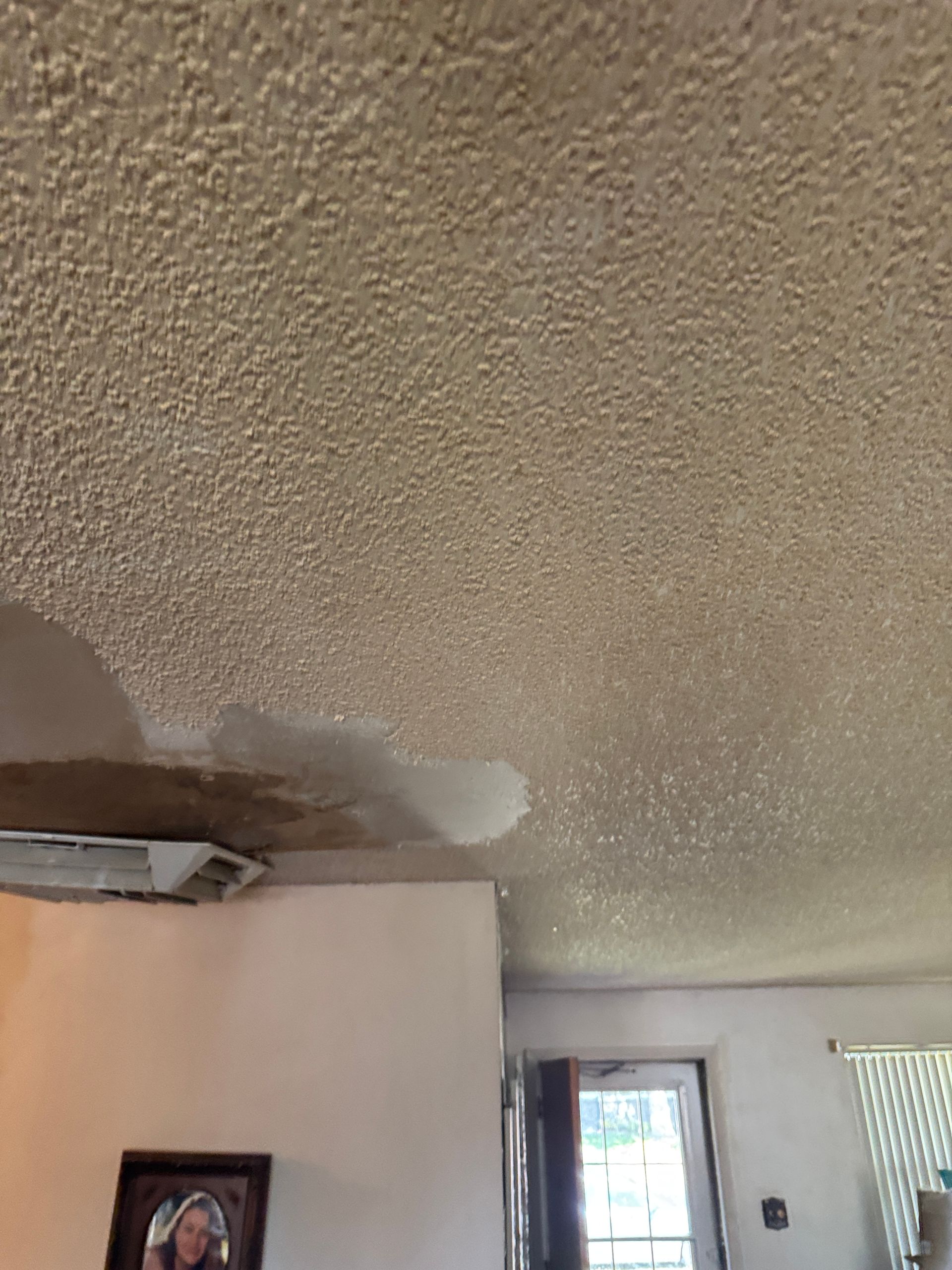 Water-damaged popcorn ceiling with visible staining and potential leakage near a wall with a light fixture and an open doorway.