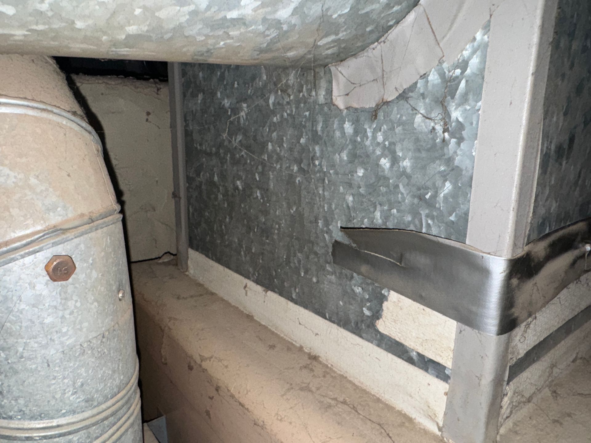 Galvanized metal ductwork and a rectangular metal box within an enclosed space.