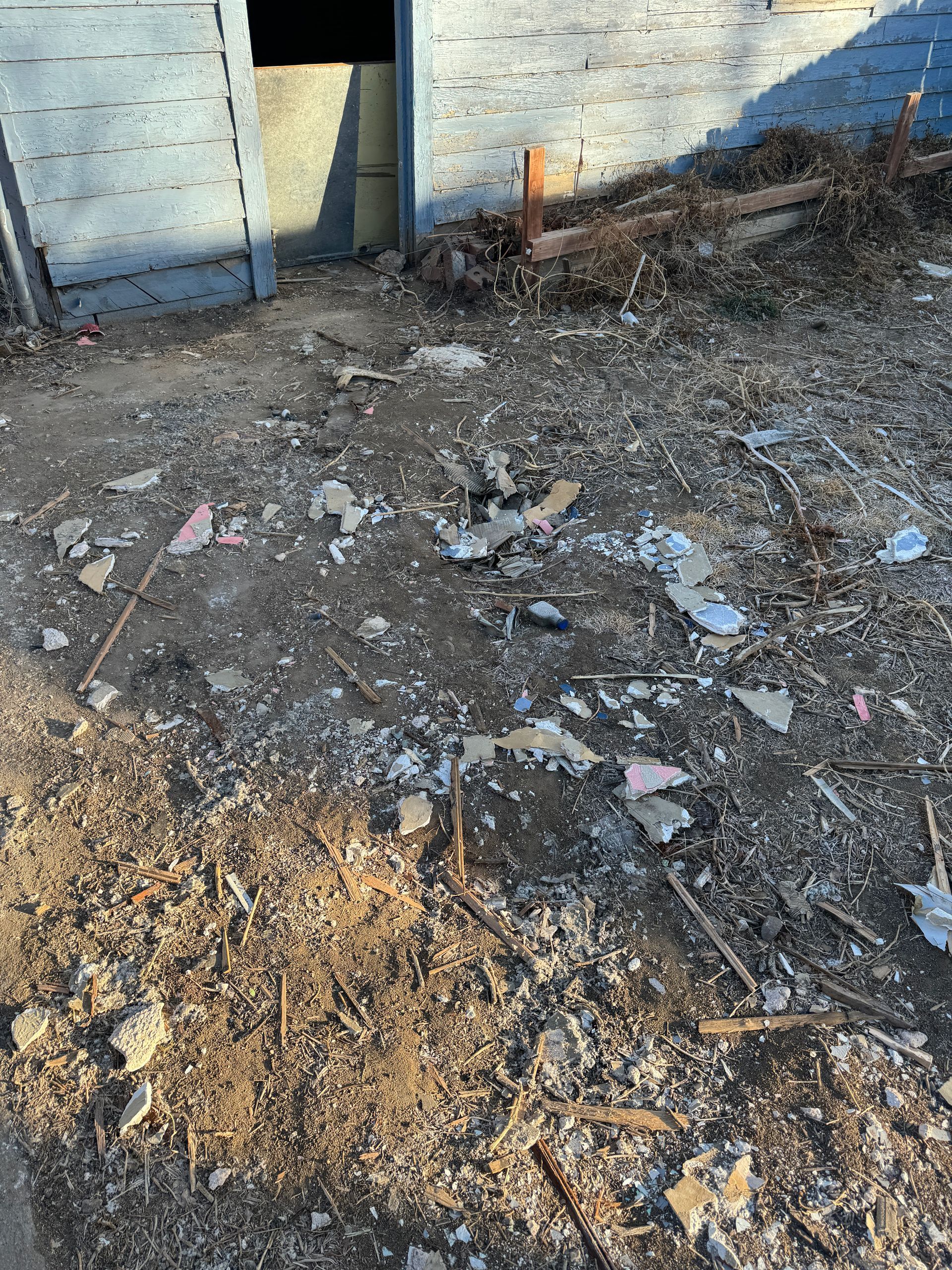 Debris and trash littered in front of a blue building with open door. Earthy tones dominate the scene.