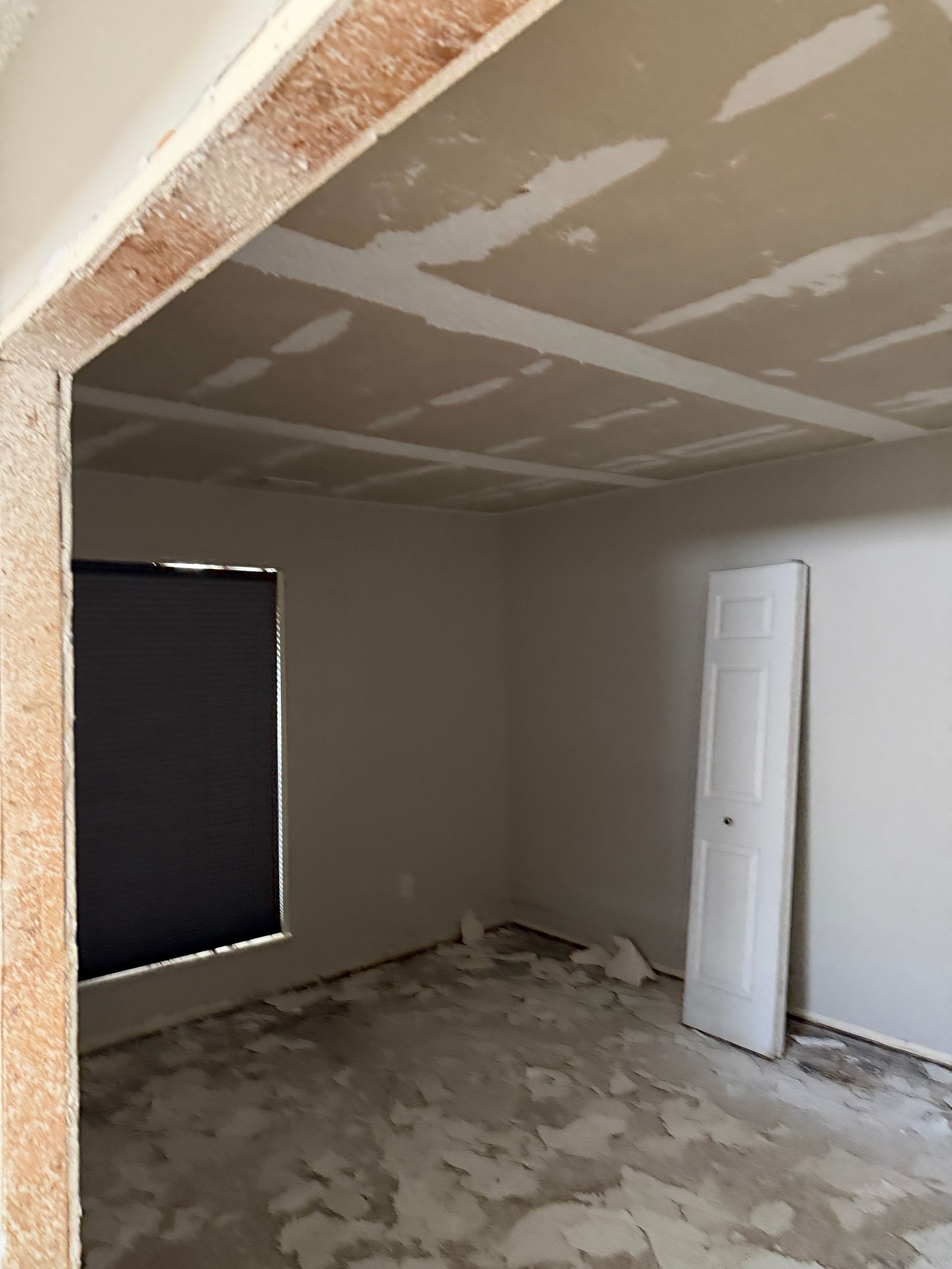 Interior of a room under construction with unfinished walls, ceiling, and doorway; a door and window are present.