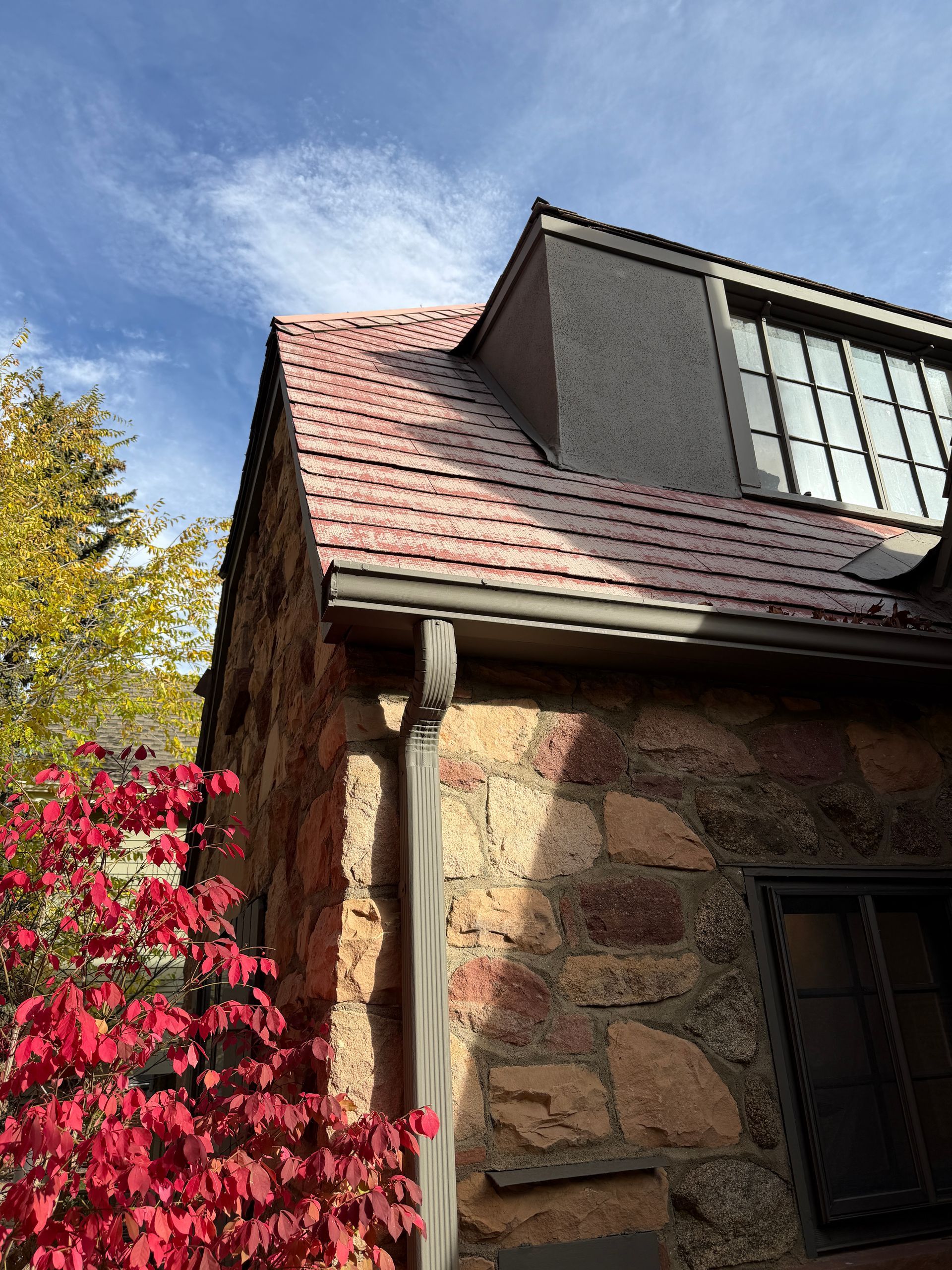 Stone building with a red-tiled roof and red fall foliage against a blue sky.