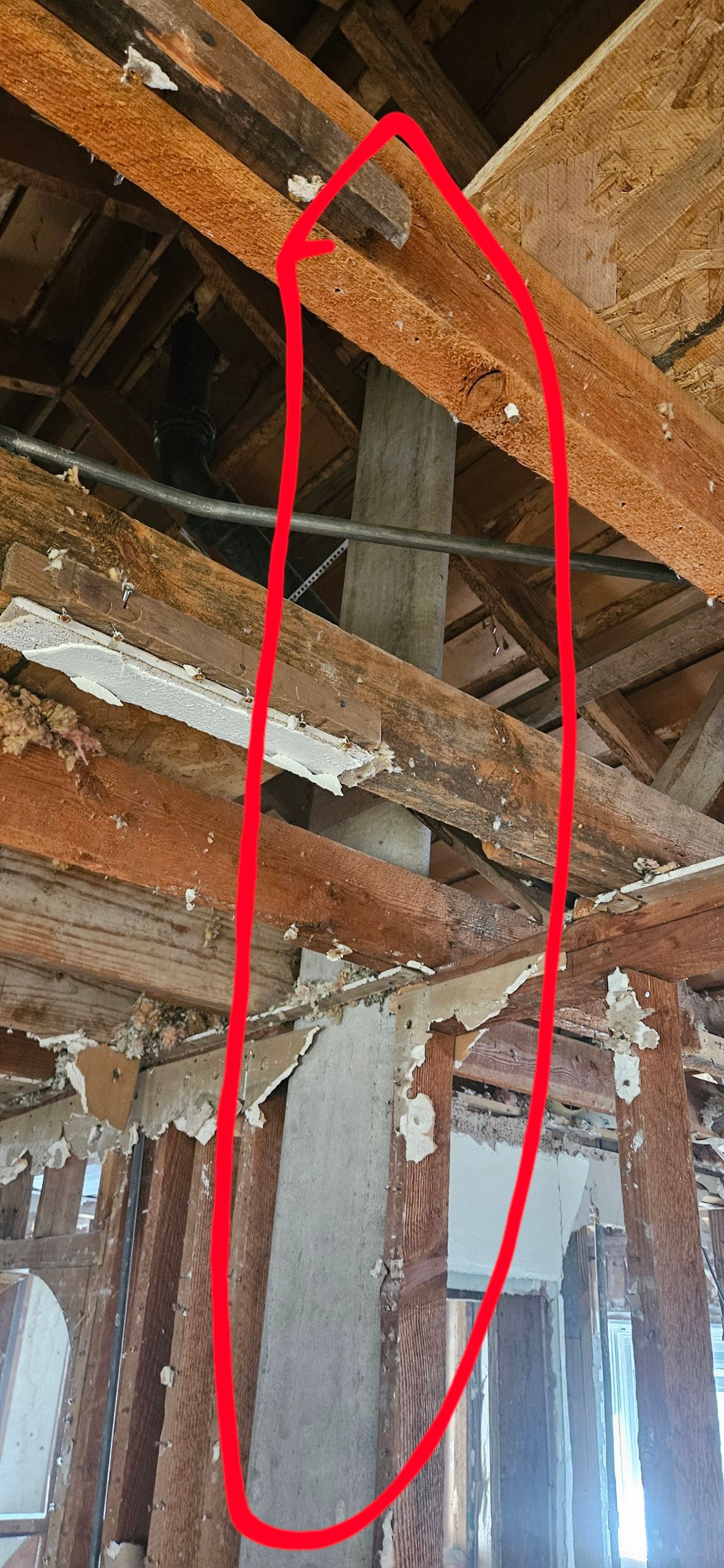 A structural beam in a damaged house, surrounded by wooden beams, and a gray concrete structure.