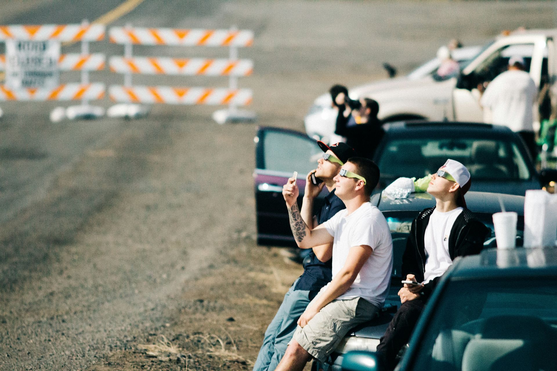 People sitting on cars and wearing eclipse glasses.
