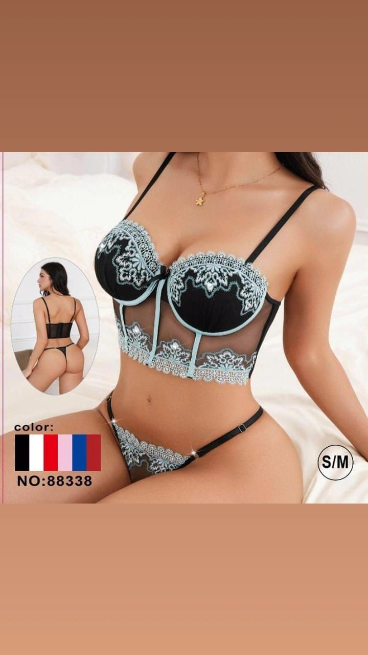 Modelo con lencería de encaje negro con bordados azul claro, posando sobre un fondo pálido.