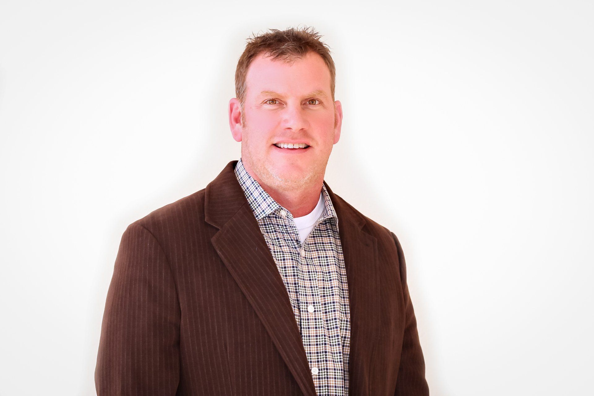 a man in a brown jacket and plaid shirt is smiling for the camera