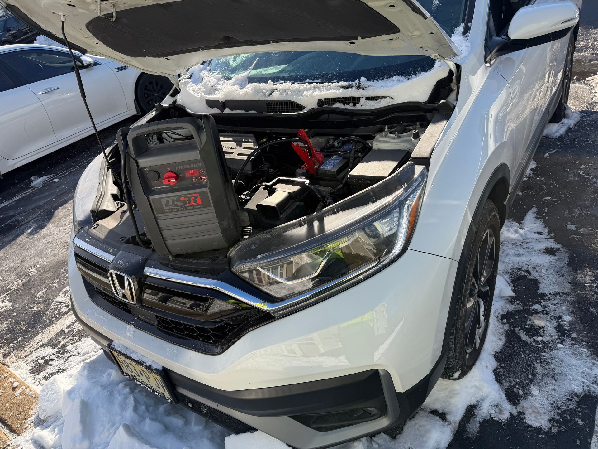 Silver car with hood open, exposing a battery in the engine bay after apparent front-end damage.