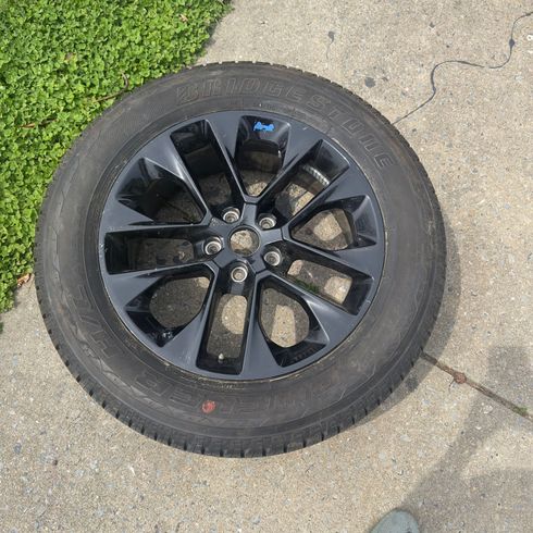Black alloy car wheel with tire lying on a concrete driveway beside grass.