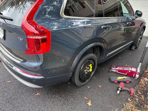 Gray SUV with a flat tire, a red jack and tools on the wet roadside