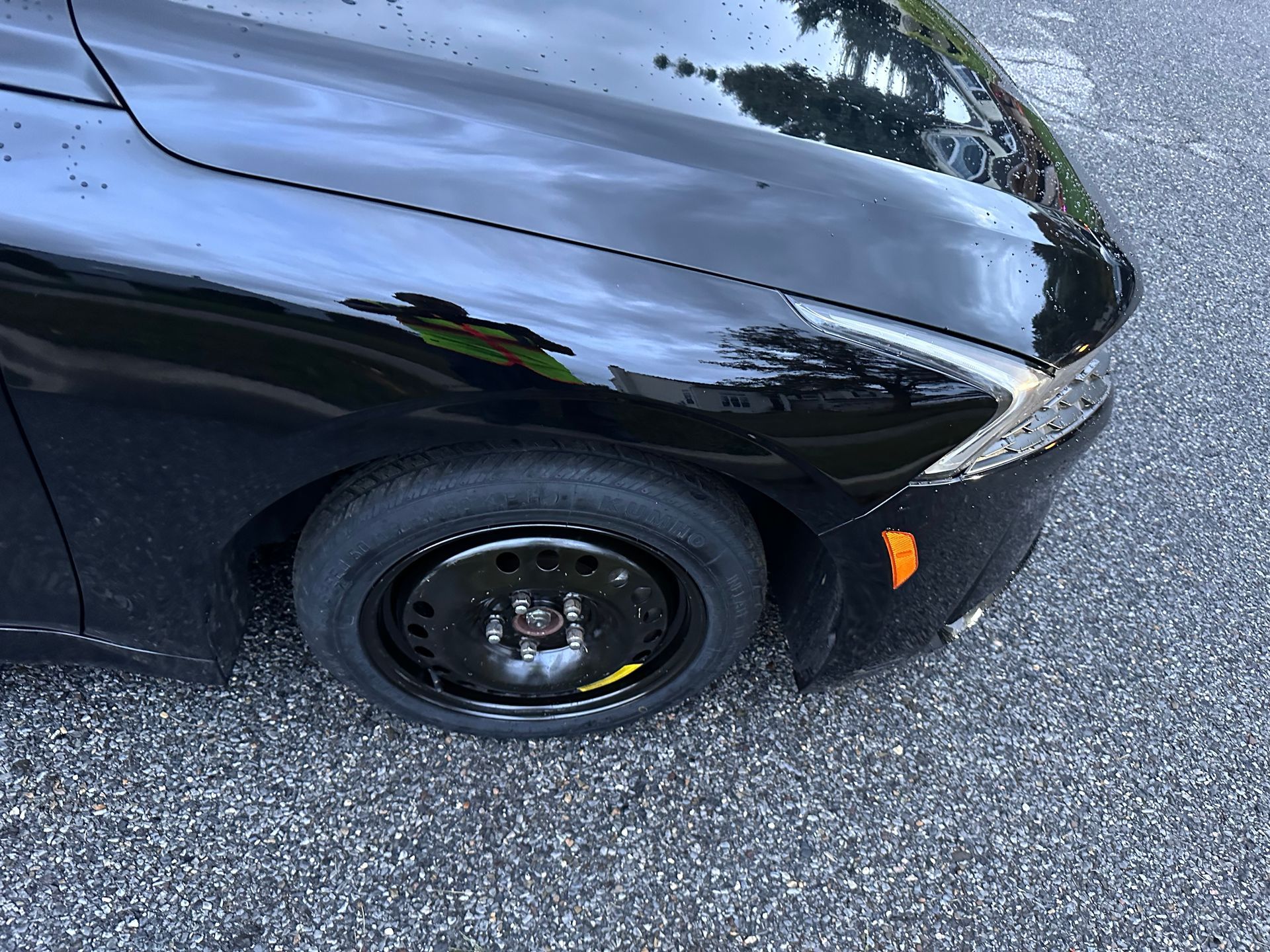 Black car with a flat front tire on a gravel road