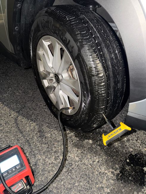 Car tire being inflated at night beside a portable air compressor and yellow chock on wet pavement