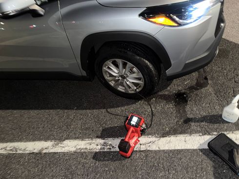 Silver SUV with front tire damage on a wet road, next to a red cordless tool and debris