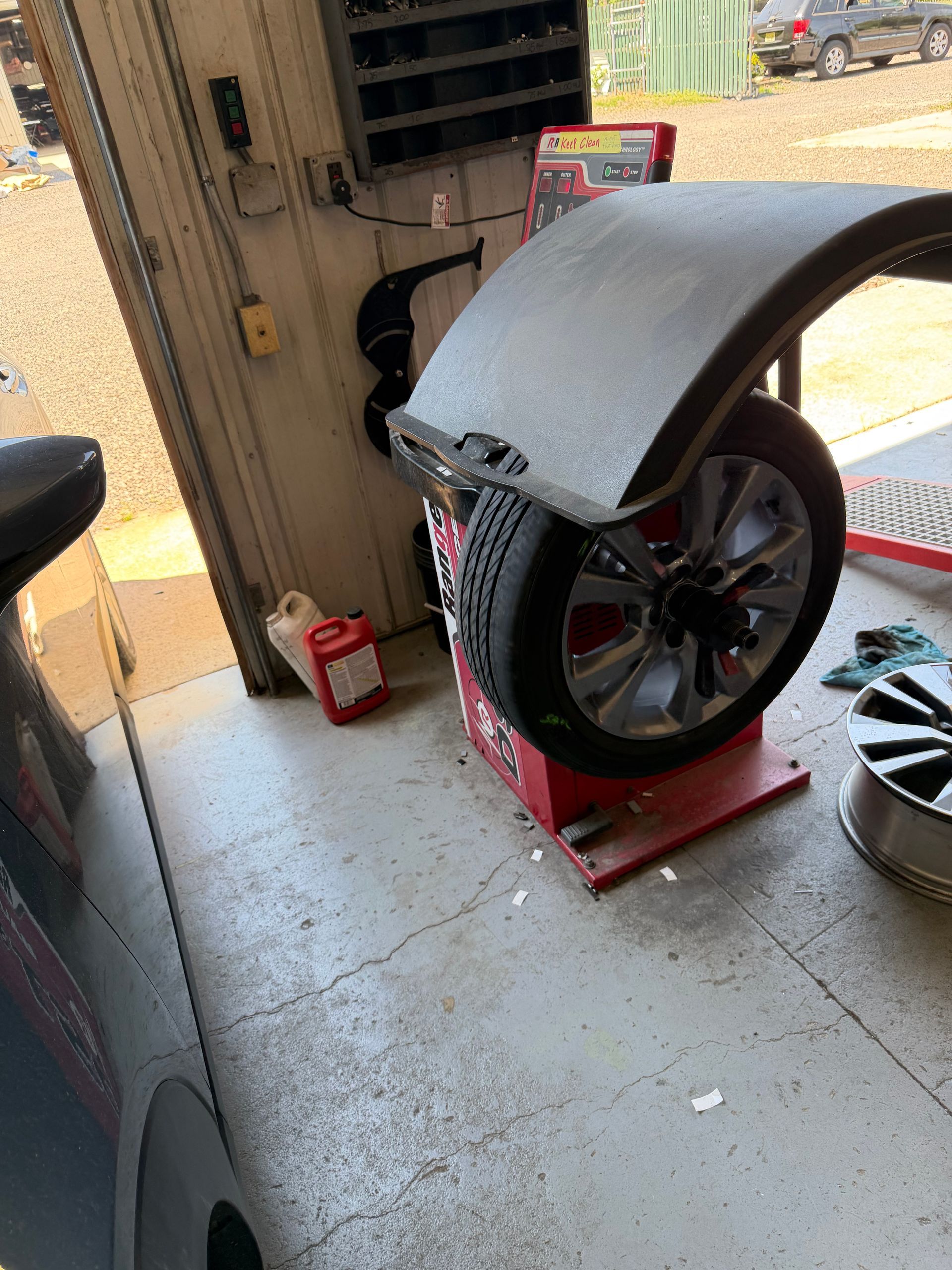 Tire balancer in a garage, with a car wheel mounted under a curved gray cover.