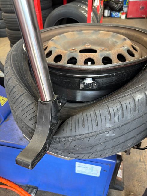 Stacked tire and steel wheel rim in a garage, with a metal tool in the foreground.