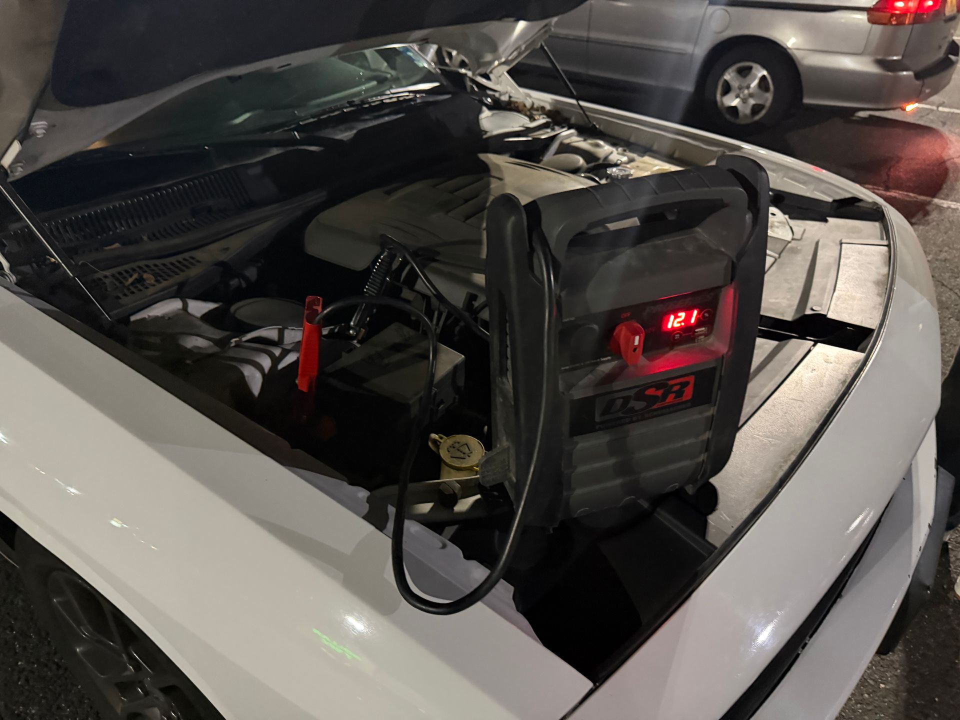 White sports car with rear engine exposed and a battery pack strapped on top, parked at night