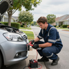 Mechanic jump-starting a silver car with jumper cables on a suburban street