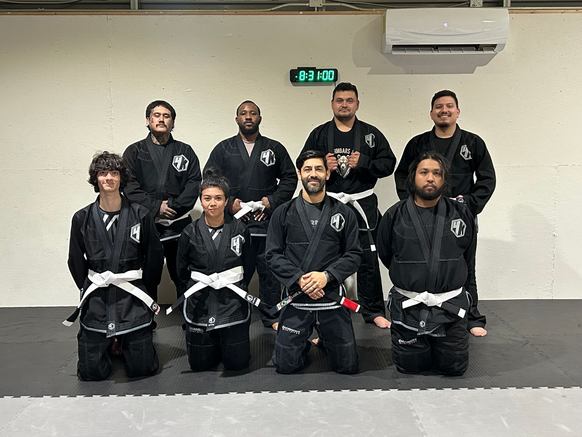Martial arts group in black gis posing in a dojo, 4Korners Jiu-Jitsu in Princeton, TX, some kneeling and some standing in two rows.