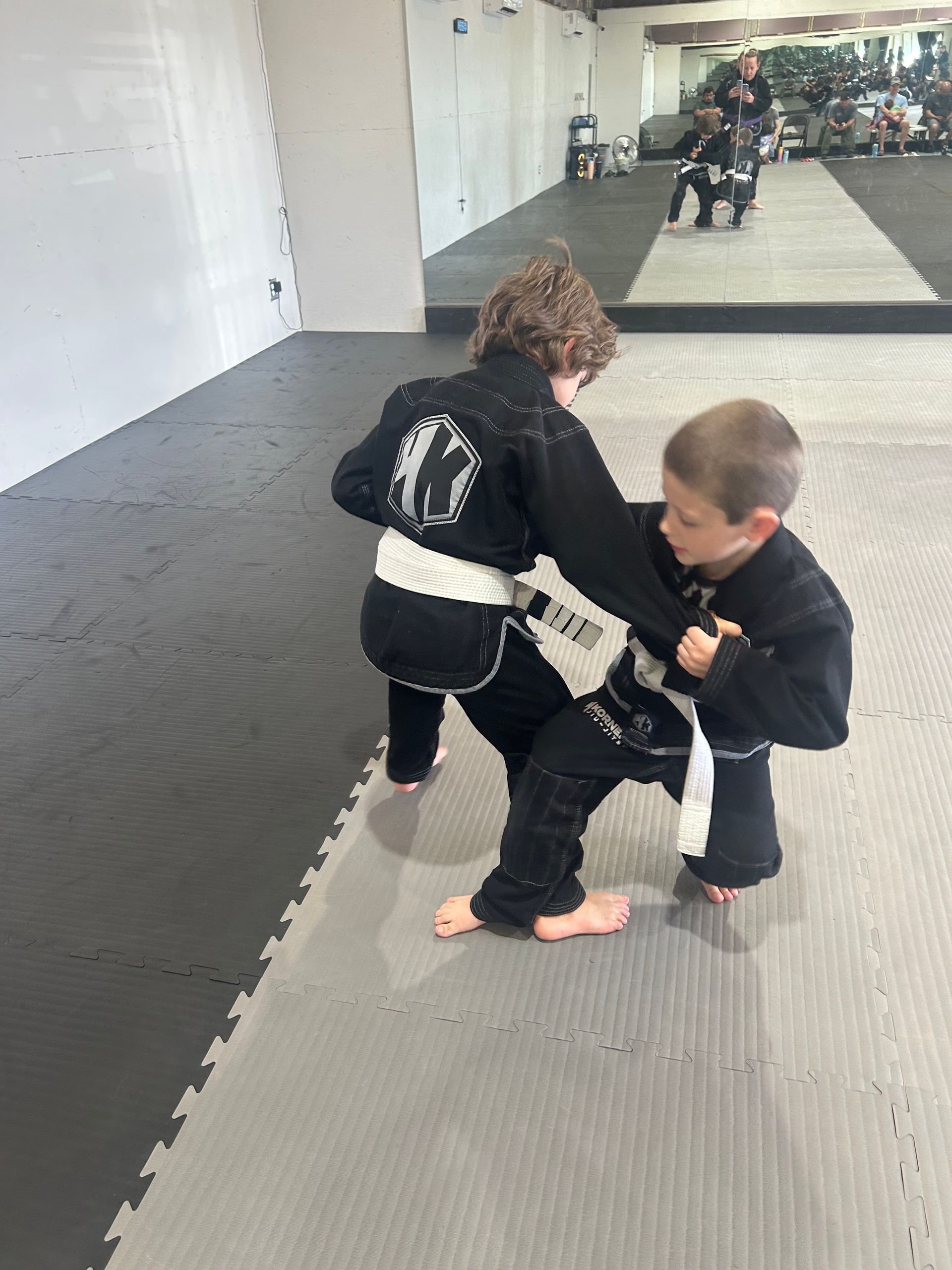 Two children practicing grappling on a padded martial arts mat in 4Korners Jiu-Jitsu in Princeton, TX