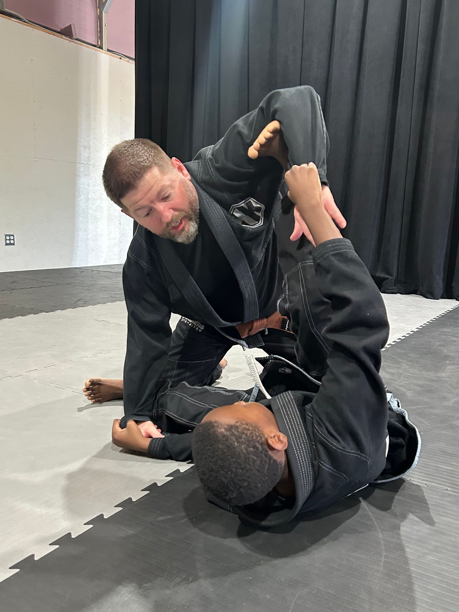 People in black martial arts uniforms lined up in 4Korners Jiu-Jitsu in Princeton, TX with white mats