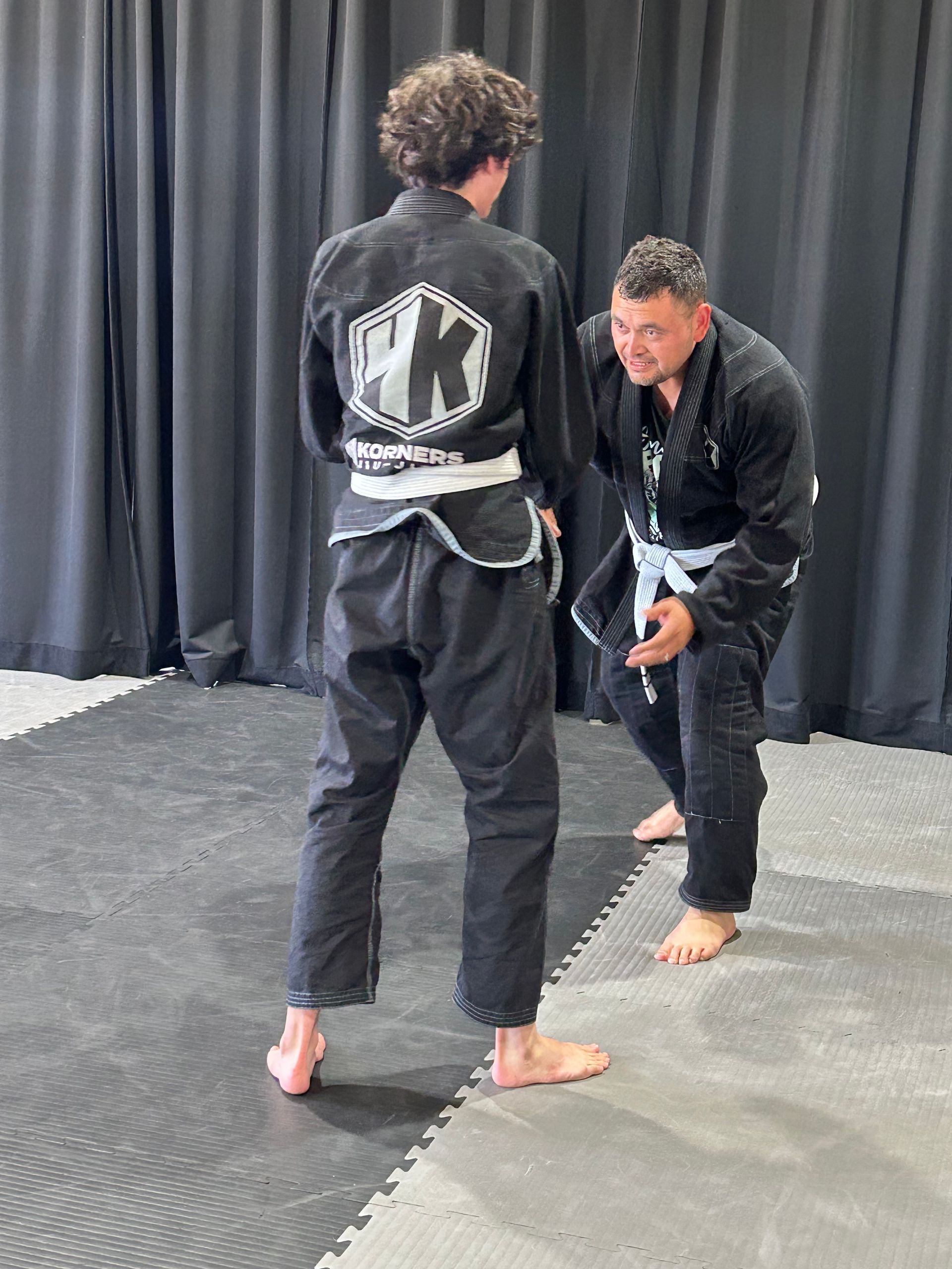 Instructor demonstrating a martial arts move in 4Korners Jiu-Jitsu in Princeton, TX, with a student practicing in the background.