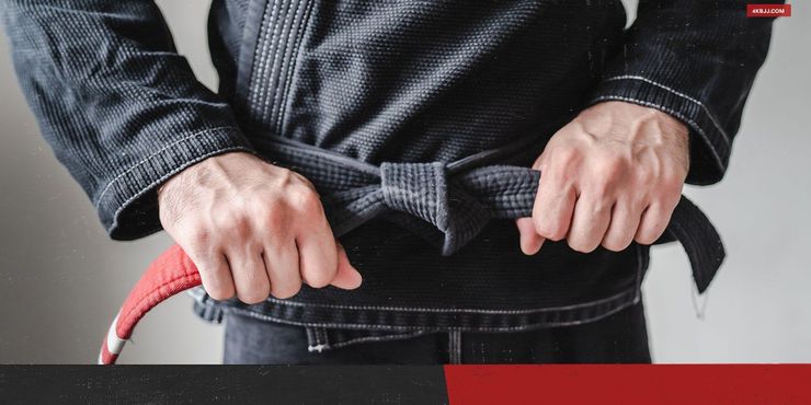 Person in a black martial arts uniform gripping a red rope or belt tied around the waist