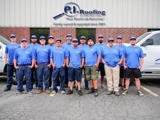 A group of people in matching blue t-shirts and hats standing in front of the P.I. Roofing office building.
