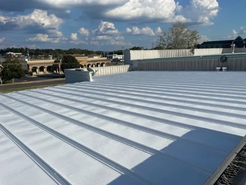 A white metal roof under a bright, partly cloudy sky, with a commercial building visible in the background.
