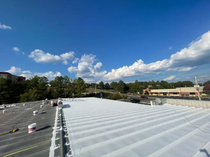A commercial roof partially covered in white roofing material against a bright blue sky with clouds.