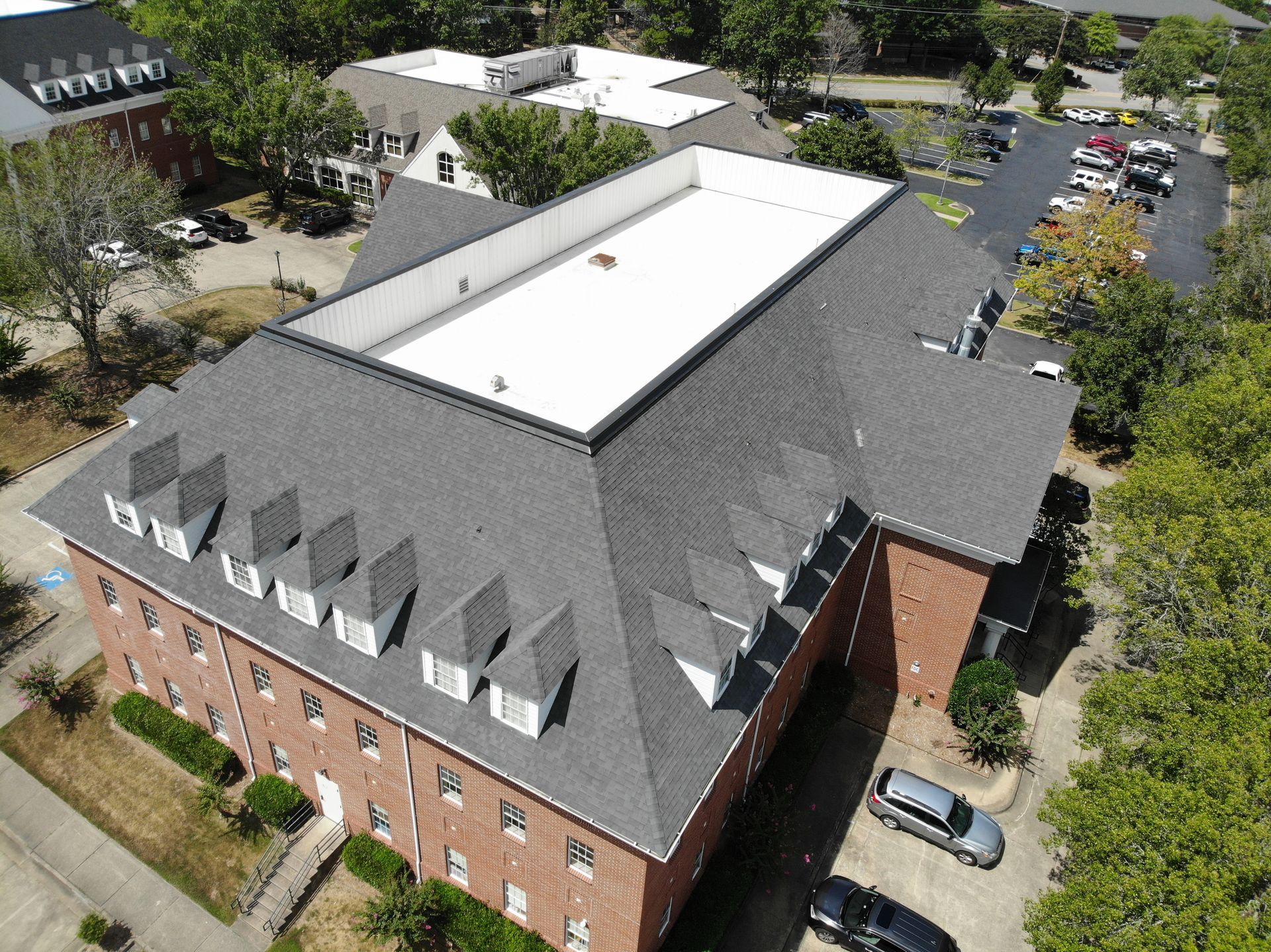 Aerial view of a multi-story brick building with a dark shingled roof featuring dormer windows and a flat white center.