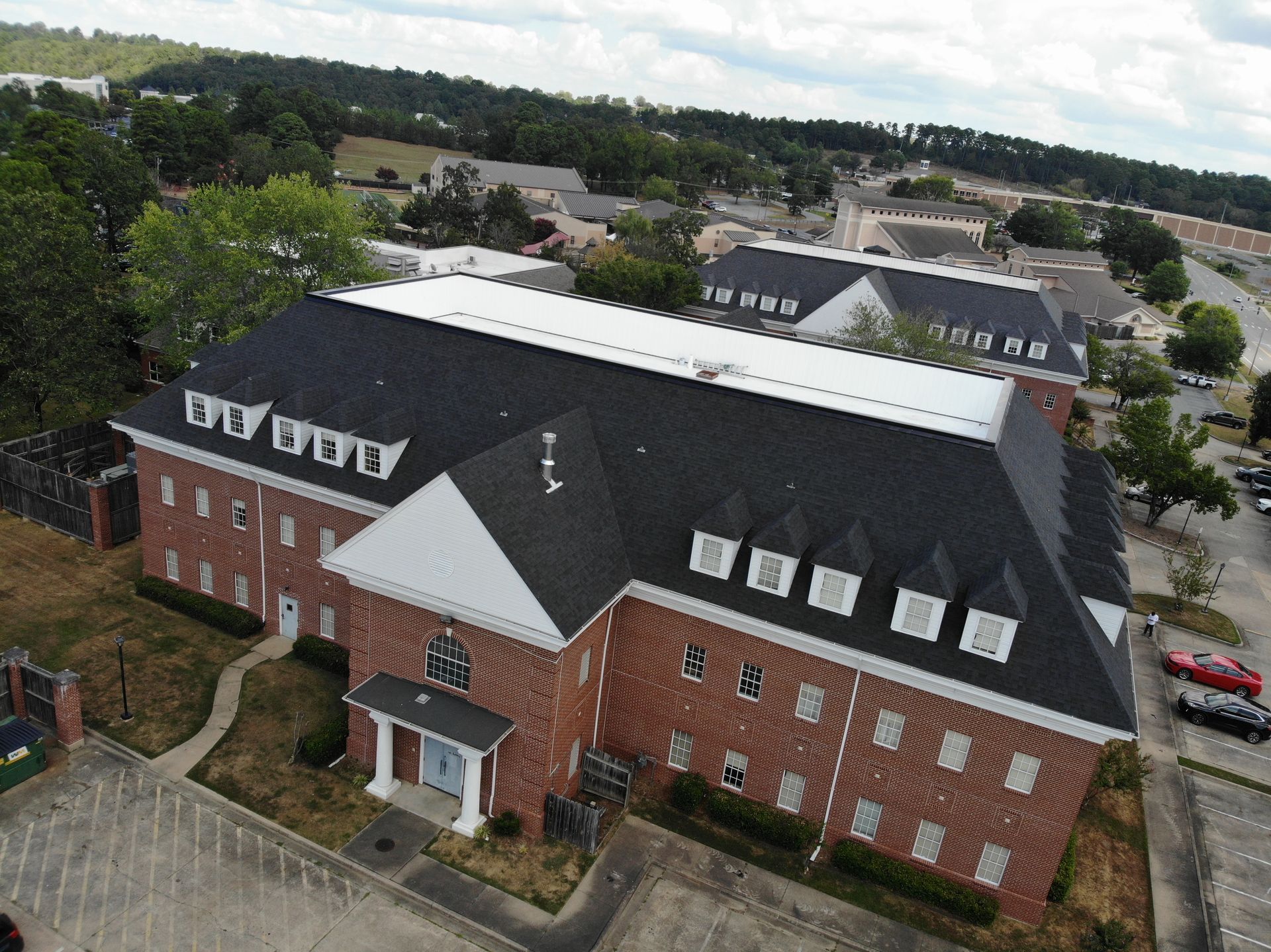 Aerial view of a multi-story brick building with a dark, shingled roof, dormer windows, and a white entrance portico.