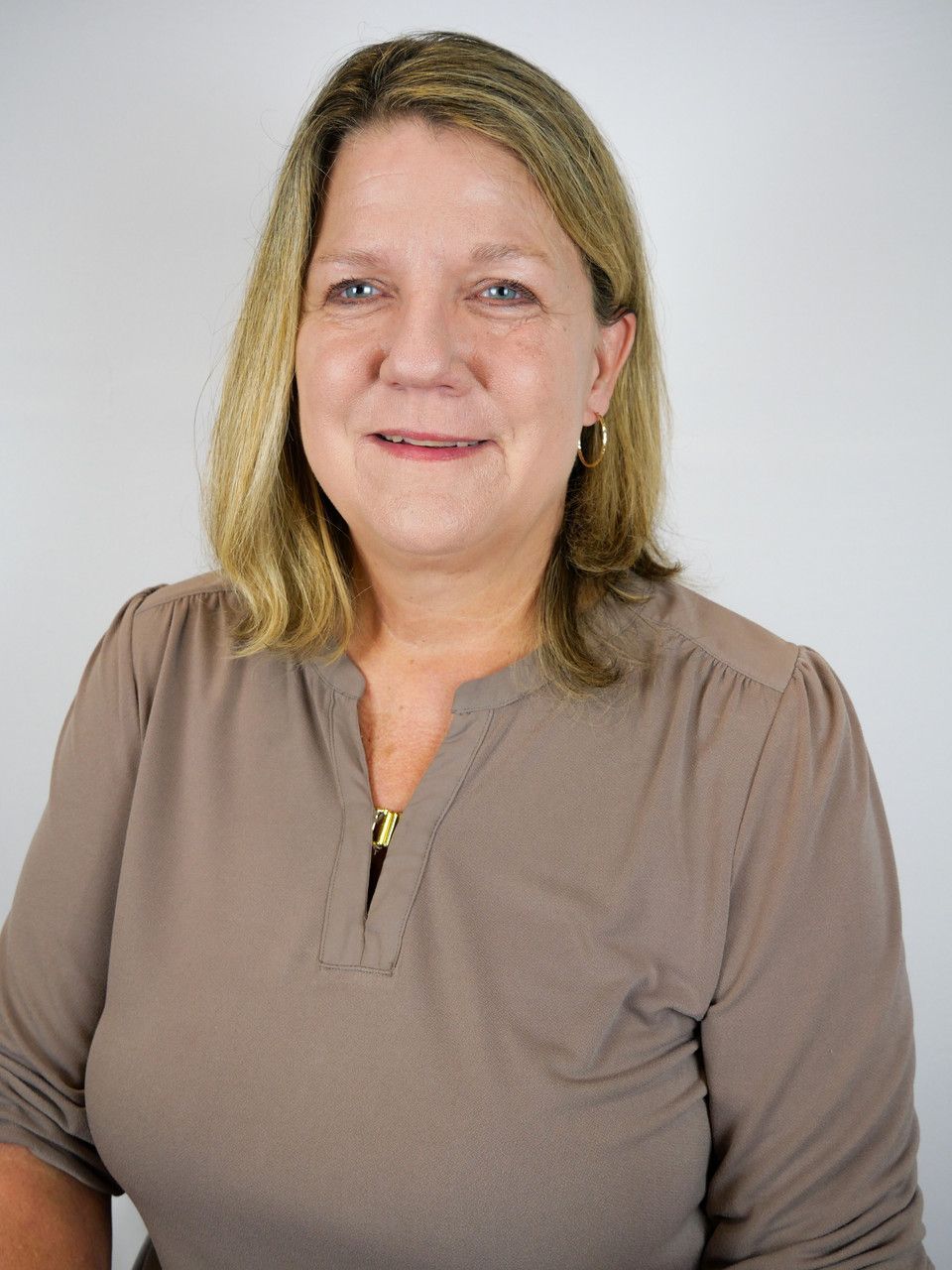 A person with shoulder-length blonde hair wearing a brown shirt, centered against a plain white background.