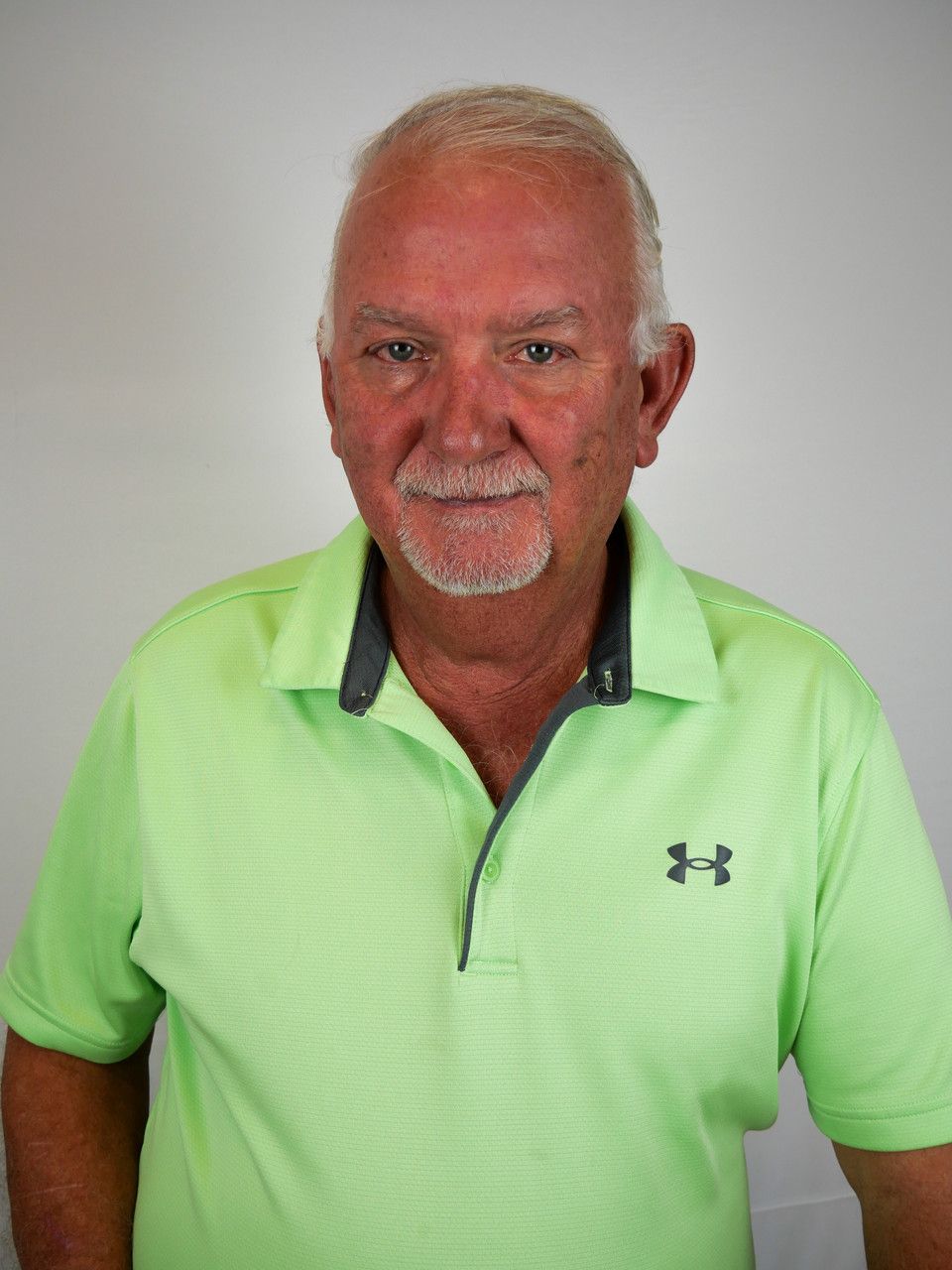 A person wearing a bright green Under Armour polo shirt with a gray collar against a plain white background.