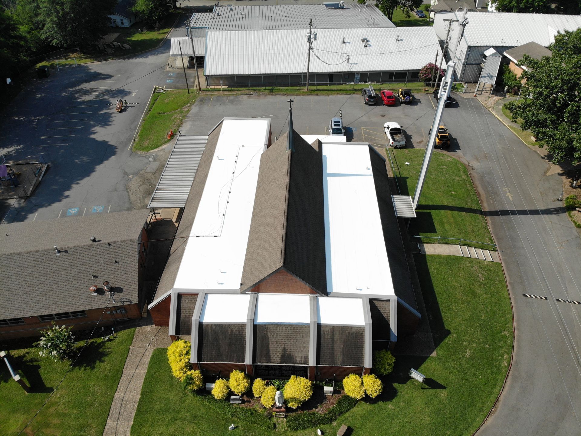 Aerial view of a church building with a brown roof, partially covered in white roofing materials, next to a parking lot.