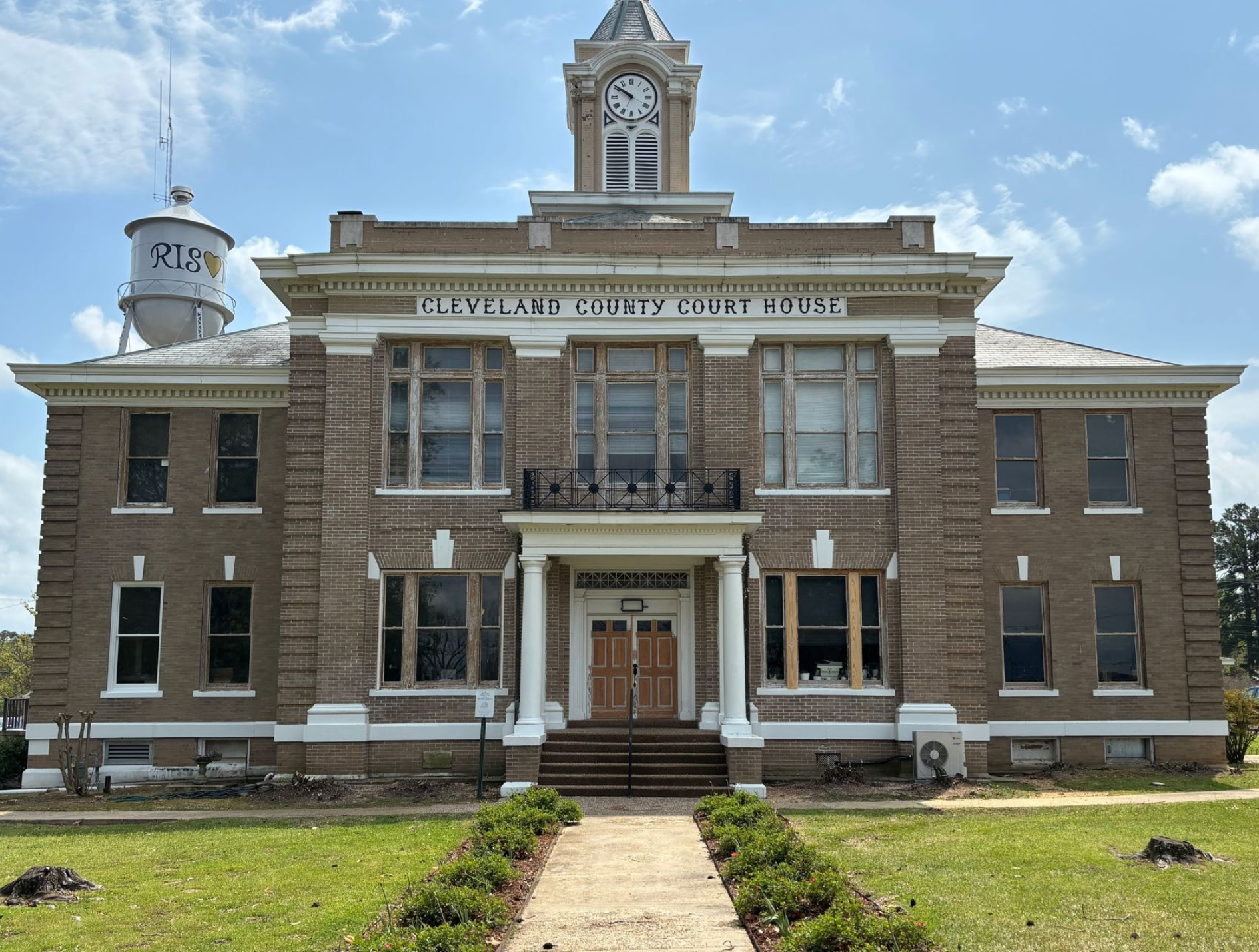 A historic brick courthouse building with a clock tower and an adjacent water tower under a blue sky.