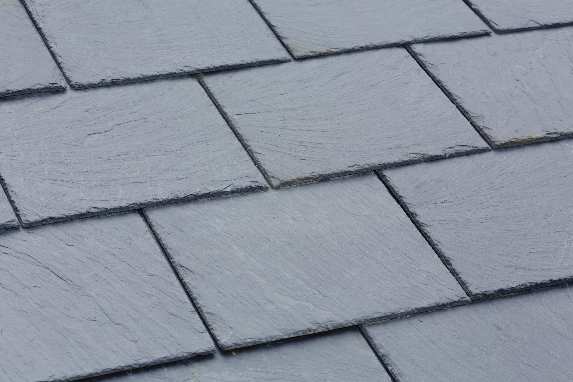 Close-up view of overlapping, rectangular dark gray slate roof tiles arranged in a staggered pattern.