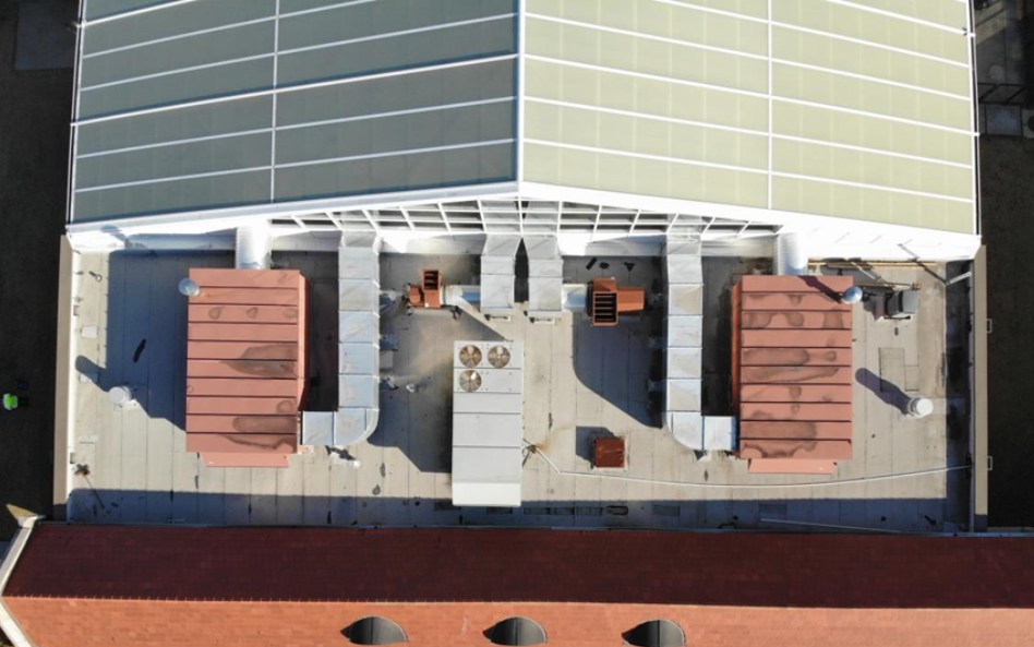 An aerial view of a building roof featuring large mechanical HVAC units, ductwork, and solar panels on a sloped section.