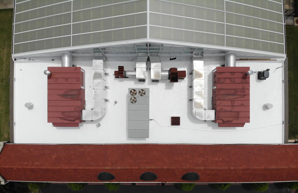 Aerial view of a flat white roof featuring solar panels, two red-topped industrial HVAC units, and silver metal ductwork.