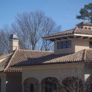 A beige stucco house with a tiled roof, architectural chimneys, and arched entryway under a clear blue sky.
