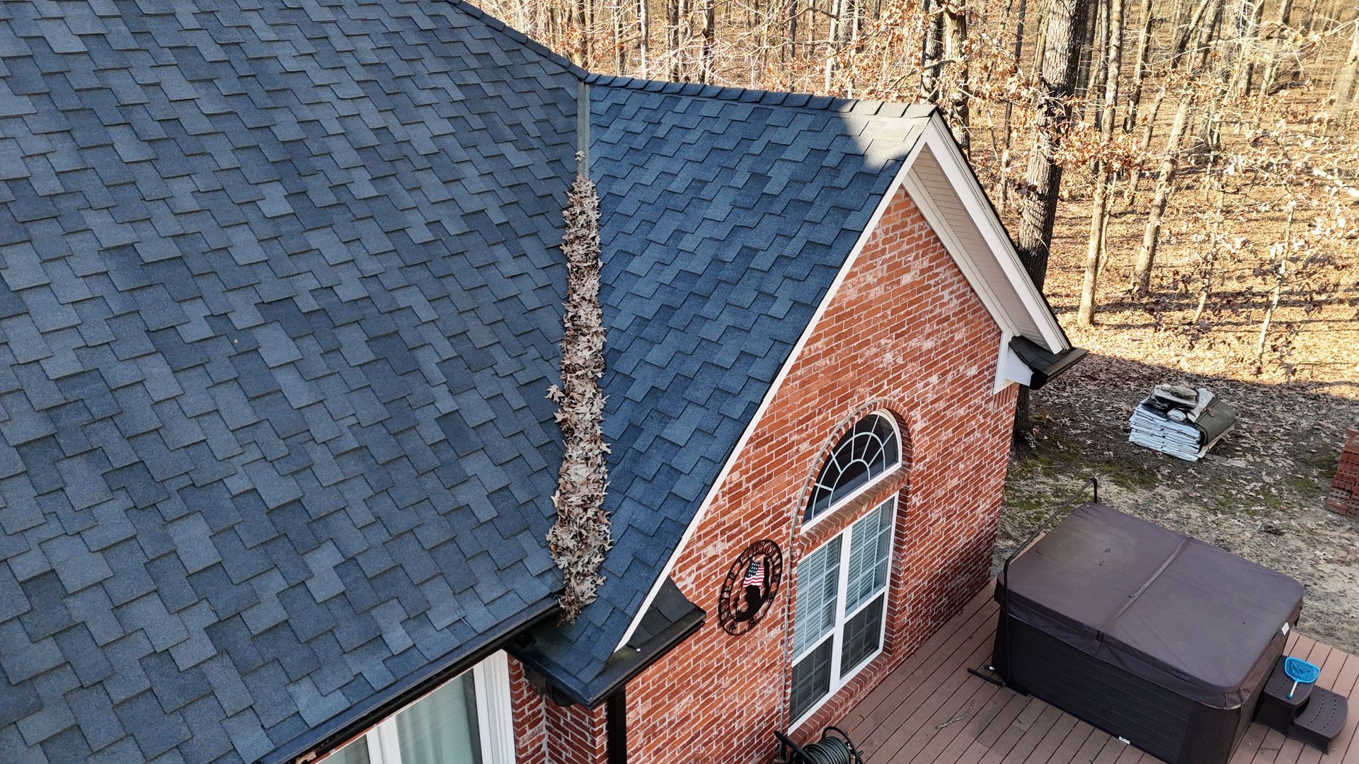A roof valley on a brick house is heavily clogged with fallen leaves, indicating a need for cleaning.