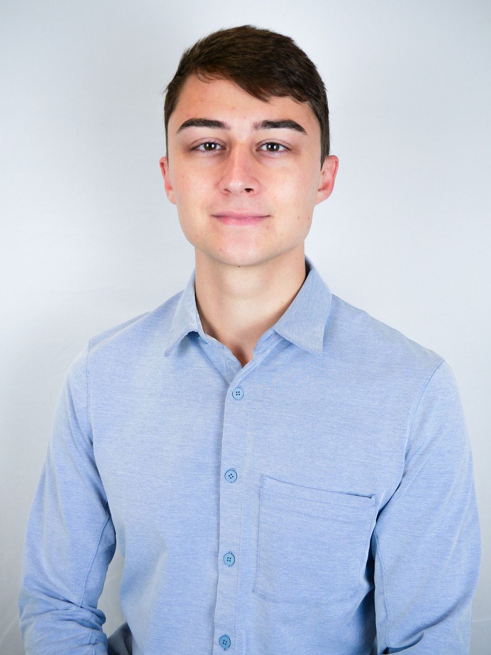 A person wearing a light blue button-down shirt stands against a plain white background, facing forward.