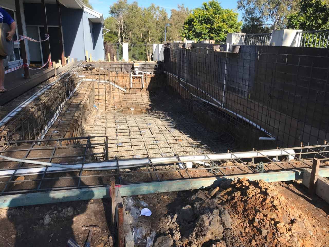 Pool under construction with exposed rebar and plumbing.