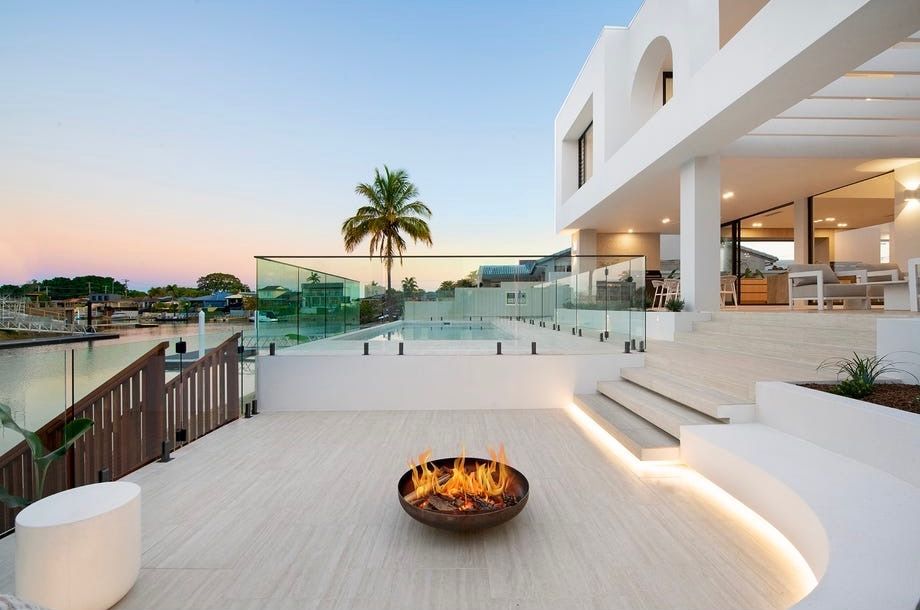 Modern patio with fire pit, white steps, glass railing, and sunset ocean view